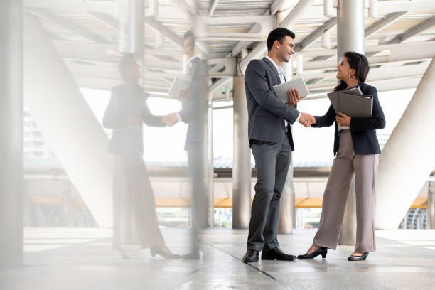 Indian businessman greeting and making handshake with a businesswoman outdoors in city walkway
